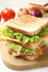 Tasty sandwich with ham, bacon, cheese and vegetables on white table, closeup