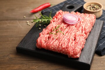 Raw minced meat with rosemary, thyme and spices on wooden table, closeup