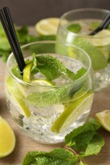 Glasses of tasty cocktails with lime and mint on wooden table, closeup