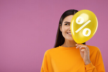 Woman holding yellow balloon with percent sign on pale purple background. Discount offer