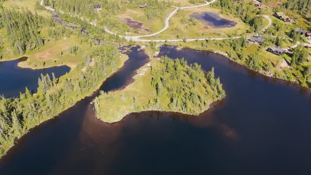 High-Angle Aerial Top-Down Shot of a Forested Lake Peninsula with Small Boats, Cabins, and Winding Roads in a Mountainous Landscape