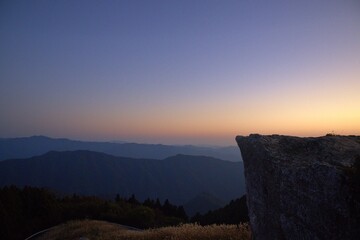  夕焼け空と山並みを見下ろす巨岩の先端
