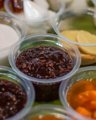 Close-up of Indonesian sweet black glutinous rice porridge (bubur ketan hitam) served in a plastic cup with other traditional desserts