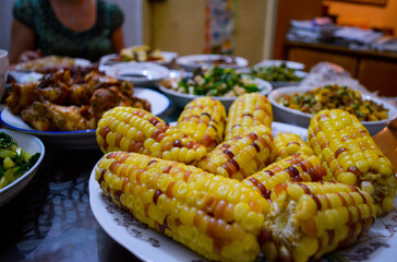 Chinese family meal on table with corn on cobs at foreground.