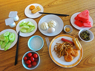 Traditional Chinese Breakfast on Wooden Table, including Steamed Buns, Rice Porridge, Fried Dough Sticks, Boiled Egg, Tofu Bean Curd and Pickled Veggie.