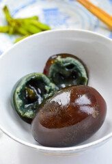 Chinese century eggs in a white bowl. One egg cut in half shows black soft yolk inside.