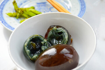 Chinese century eggs in a white bowl. One egg cut in half shows black soft yolk inside.