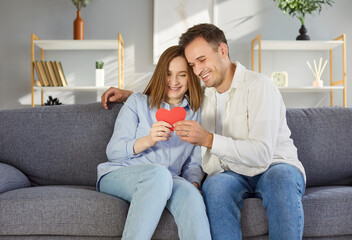 Happy couple, young people in love at home, smiling man and woman holding red heart symbol on happy...