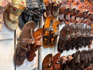 handcrafted leather sandals, likely Kolhapuri chappals, hanging for sale. The sandals are arranged in multiple rows and columns, showcasing a variety of designs and shades of brown leather.