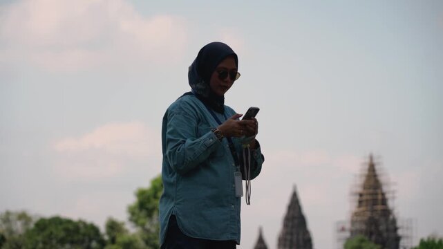Asian muslim women solo traveler using smartphone taking photos at Prambanan temple, Central java, Yogyakarta, Indonesia with his smartphone. Solo travel concept.