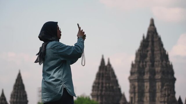 Asian muslim women solo traveler taking photos at Prambanan temple, Central java, Yogyakarta, Indonesia with his smartphone. Solo travel concept.