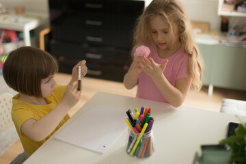 Baby girl sits at a table at home, engaged in an educational activity. Child concentrates on writing or drawing on a sheet of paper. Early childhood development, learning through play, and creativity.