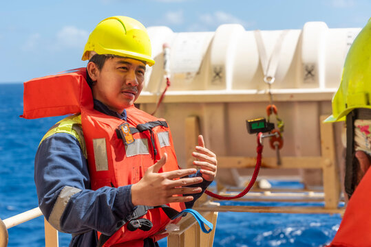 Deck officer wearing a yellow hard hat and orange life jacket demonstrates life raft deployment on a merchant ship. 