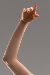 Woman's arm reaching upward with index finger pointing on gray background