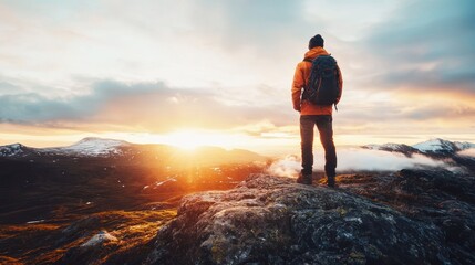 A man standing on a rocky outcrop overlooking a mountainous landscape at sunset.
