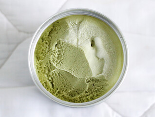 Matcha ice cream in a plastic container on a white tablecloth background