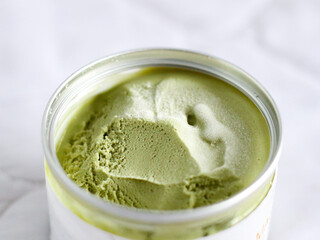 Matcha ice cream in a plastic container on a white tablecloth background
