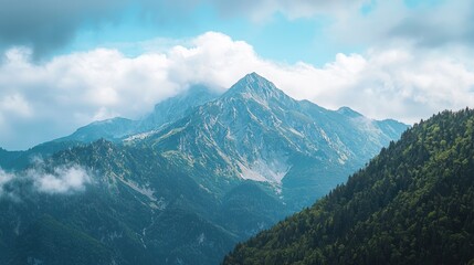 Obraz premium A majestic mountain range with lush green forests and a cloudy sky in the background.