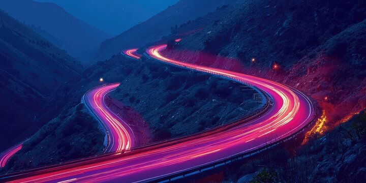 A winding road with colorful lights at night, set against a mountainous backdrop with a fire in the foreground.