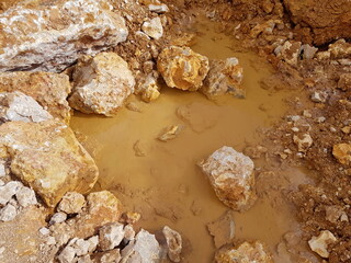 Muddy water collects in a dirt hole, surrounded by various brown and white stones. An excavation site after rain