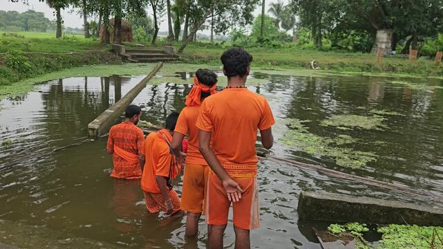 Authentic footage of Kanwariya devotees dressed in saffron clothing collecting holy water from a village pond during the sacred Shravan Somwar Sawan Monday pilgrimage in India.