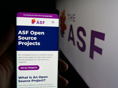 Stuttgart, Germany - 10-08-2025: Person holding smartphone with web page of organisation Apache Software Foundation (ASF) on screen in front of logo. Focus on center of phone display.