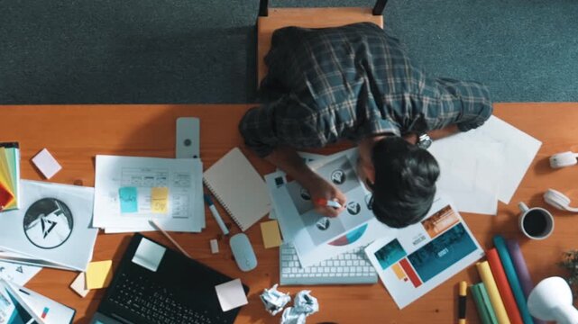 Top view of designer writing and designing logo graphic at meeting. Closeup of business man working on colored palettes and writing idea on sticky notes on table with equipment and paper. Symposium.