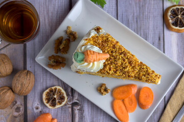 Top-down view (flat lay) of a slice of carrot cake with walnuts, fresh carrots, and a cup of hot...