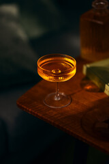 Close-up of an elegant cocktail glass filled with an amber drink, bathed in warm evening light on a wooden table. A cozy and sophisticated still life scene.