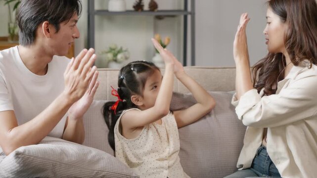Family fun time parents and child playing clapping game at home cozy living room joyful interaction warm atmosphere
