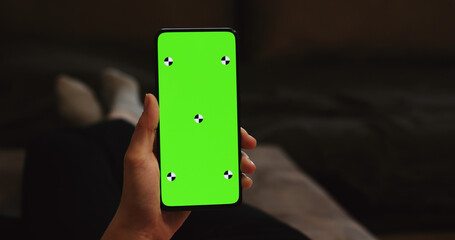 young woman lying on a couch and holding smartphone with vertical green screen