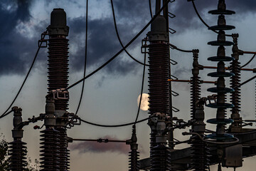 An electrical substation operates at night under a bright full moon. Power lines, transformers, and glowing lights create a dramatic scene symbolizing energy supply, infrastructure, and reliable elect