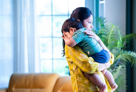 Indian Mom gently holding sleeping infant boy on shoulder, bonding quietly in bright modern home