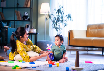 Indian Mother and infant boy playing ring toys on carpet together in bright modern home