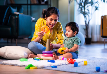 Indian Mother and infant boy playing ring toys on carpet together in bright modern home
