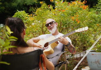 A man plays guitar for a woman near a cozy tent at a glamping site.