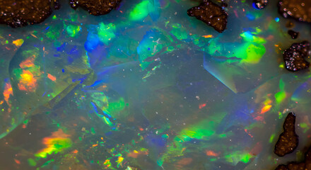 Iridescent opal stone with spectrum of colors exhibits a luminous, ethereal quality, showcasing a harmonious blend of blues, greens, reds and oranges with a dark brown matrix providing contrast and