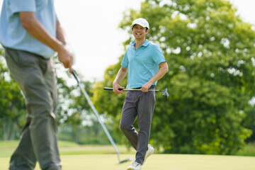 Senior and young golfers walking on fairway, discussing golf game.