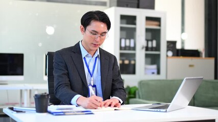 Confident Asian businessman using tablet and laptop in modern office. Perfect for business themes of technology, presentation, planning, leadership, and success. - Powered by Adobe