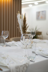 Modern restaurant interior with beautifully arranged dining table, white linen, and dried floral decor. Cozy lighting and neutral tones create an elegant dining atmosphere.
