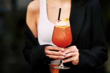 Woman holds red summer cocktail in bar close up