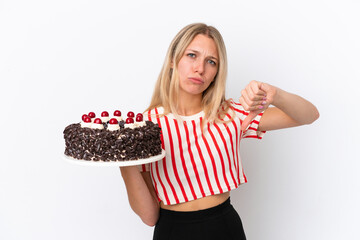 Young caucasian woman holding birthday cake isolated on white background showing thumb down with negative expression