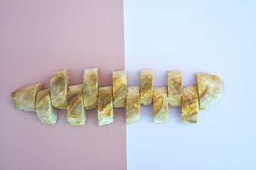 Sliced baguette arranged on pink and white pastel background. Minimal flat lay bread composition symbolizing balance, geometry and simplicity.