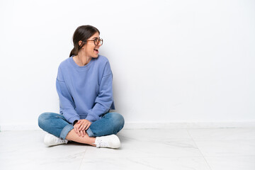 Fototapeta premium Young caucasian woman sitting on the floor isolated on white background laughing in lateral position