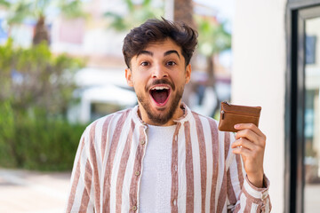 Handsome Arab man holding a wallet at outdoors with surprise and shocked facial expression