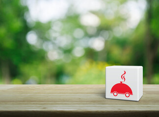 Restaurant cloche flat icon on white block cube on wooden table over blur green tree in park, Business food delivery online concept