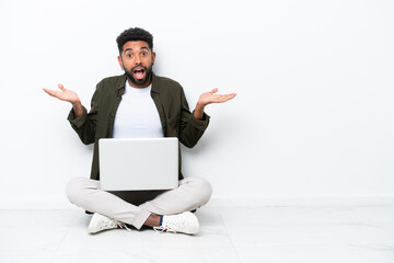 Young Brazilian man with a laptop sitting on the floor isolated on white with shocked facial expression