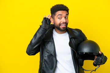 Young Brazilian man with a motorcycle helmet isolated on yellow background listening to something by putting hand on the ear