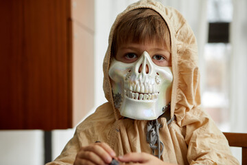 A child wearing a spooky skeleton mask along with a cozy hood is all set for some Halloween fun indoors