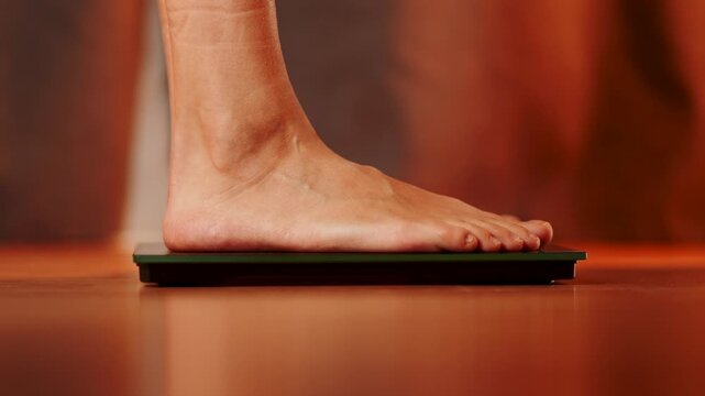 Person stepping on a scale to measure weight at home in warm lighting